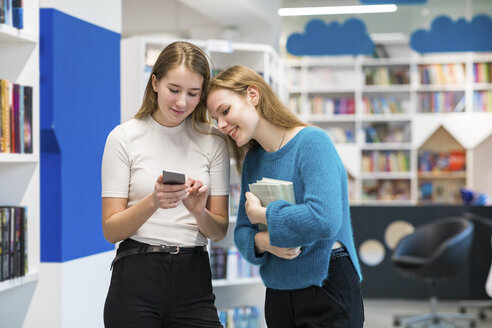 Zwei Teenager-Mädchen in einer öffentlichen Bibliothek schauen auf ihr Handy - WPEF00507