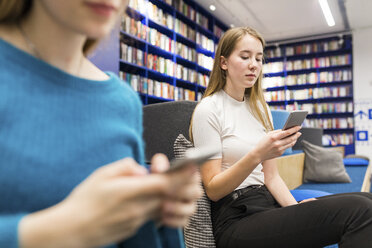 Portrait of t teenage girl sitting in a public library using cell phone - WPEF00512