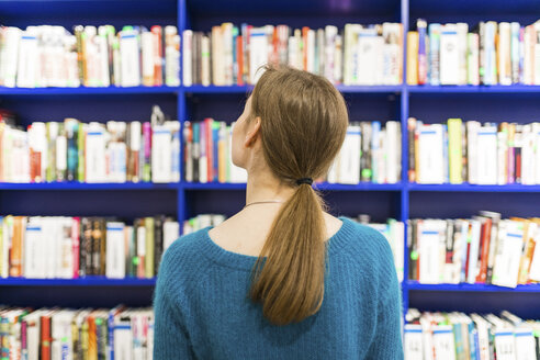 Rückenansicht eines Mädchens in einer öffentlichen Bibliothek auf der Suche nach einem Buch - WPEF00516