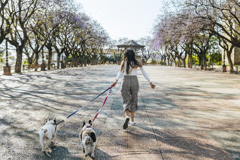 Spain, Andalusia, Jerez de la Frontera, Woman running with two dogs on square stock photo