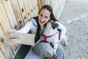 Junge Frau mit Smartphone, die ein Selfie mit ihrem Hund macht - KIJF01957