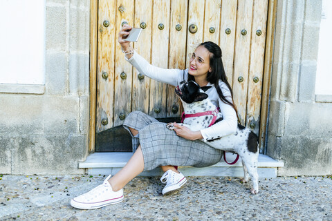 Junge Frau mit Smartphone, die ein Selfie mit ihrem Hund macht, lizenzfreies Stockfoto