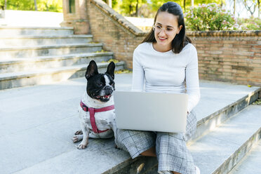 Frau mit Laptop neben ihrem Hund, auf der Treppe sitzend - KIJF01967
