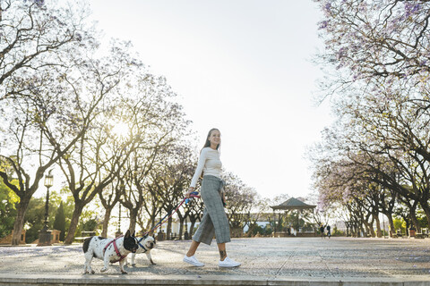 Spanien, Andalusien, Jerez de la Frontera, Frau geht mit zwei Hunden auf einem Platz spazieren, lizenzfreies Stockfoto