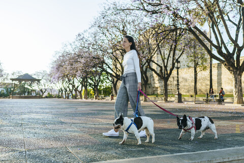 Spanien, Andalusien, Jerez de la Frontera, Frau geht mit zwei Hunden auf einem Platz spazieren, lizenzfreies Stockfoto