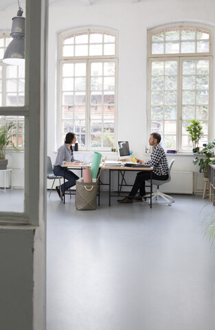 Kollegen arbeiten am Schreibtisch in einem Loftbüro, lizenzfreies Stockfoto