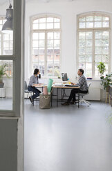 Colleagues working at desk in a loft office - FKF02954