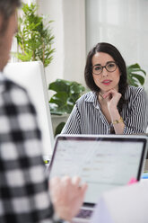 Porträt einer Frau mit einem Kollegen, der am Schreibtisch im Büro arbeitet - FKF02958