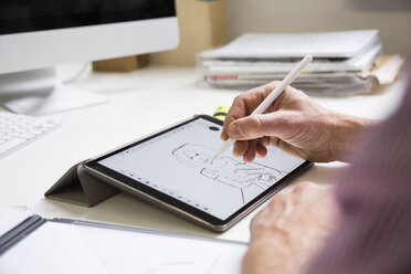 Nahaufnahme eines Mannes, der an einem Schreibtisch im Büro arbeitet und eine weibliche Figur auf einem Tablet zeichnet - FKF02970