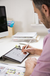 Mann arbeitet am Schreibtisch im Büro und zeichnet eine weibliche Figur auf einem Tablet - FKF02971