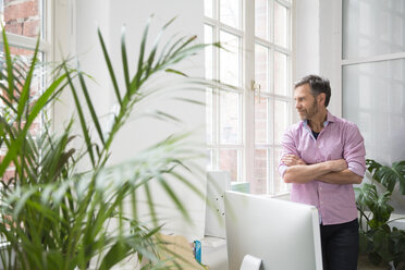 Man looking out of window in office - FKF02973