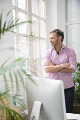 Man looking out of window in office - FKF02974