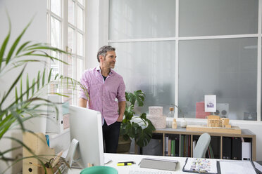 Man standing at the window in a loft office - FKF02977