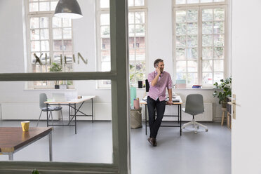 Man talking on cell phone in a loft office - FKF02978