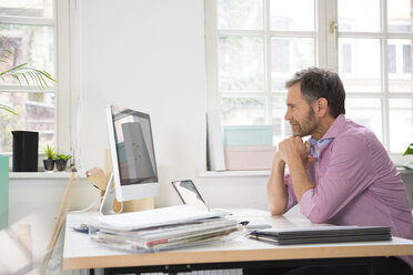 Lächelnder Mann arbeitet am Schreibtisch im Büro - FKF02980