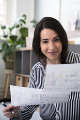 Portrait of smiling woman holding sheets of paper in office - FKF03003