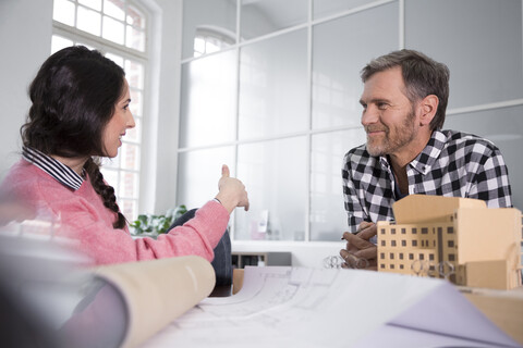 Lächelnde Kollegen besprechen ein Architekturmodell im Büro, lizenzfreies Stockfoto