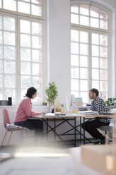 Colleagues working at desk in a loft office - FKF03015