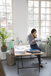Frau mit Tasse Kaffee schaut auf Papier am Schreibtisch im Büro - FKF03022
