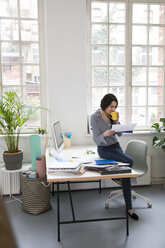 Woman with cup of coffee looking at paper at desk in office - FKF03022