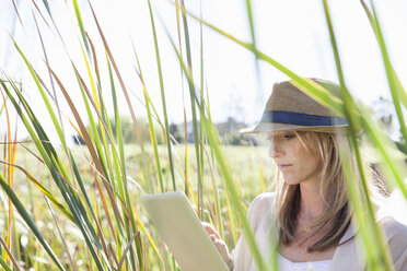 Mid adult woman sitting in long grass, using digital tablet - CUF37452