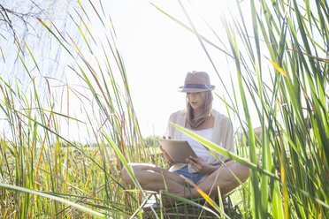 Mid adult woman sitting in long grass, using digital tablet - CUF37453