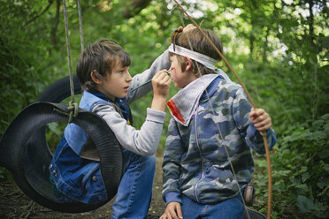 Boy face painting friend whilst playing in forest - CUF37547