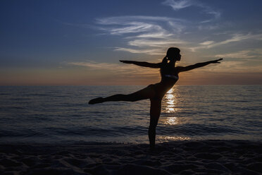 Silhouettierte junge Frau, die am Strand bei Sonnenuntergang eine Yogapose einnimmt, Oristano, Sardinien, Italien - CUF37582