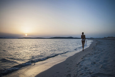 Rear view of young woman strolling on beach carrying bikini top, Cagliari, Sardinia, Italy - CUF37585