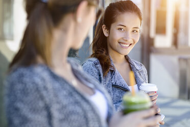 Zwei junge Frauen mit Kaffee zum Mitnehmen lehnen an einem Parkgebäude - CUF37589