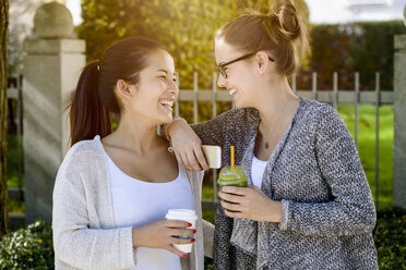 Zwei junge Freundinnen im Park lachen und trinken Kaffee zum Mitnehmen - CUF37593