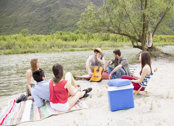 Friends sitting by river, playing guitar - CUF37720