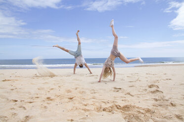 Young couple doing handstands on beach - CUF37724