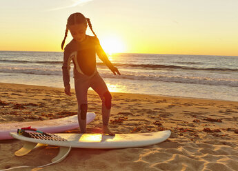 Junges Mädchen am Strand im Neoprenanzug und auf dem Surfbrett stehend - ISF14590