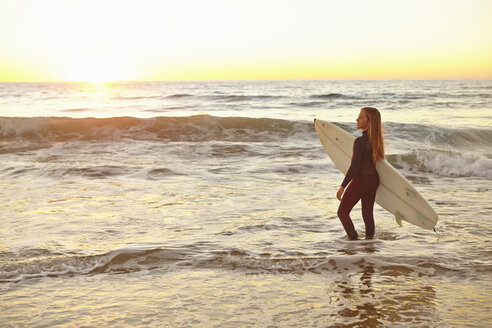 Girl carrying surfboard in sea wearing wetsuit - ISF14591