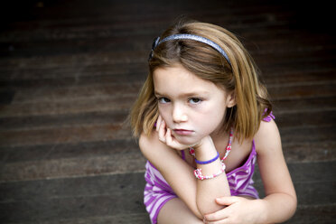 Sullen young girl sitting on porch with hands on chin - ISF14651