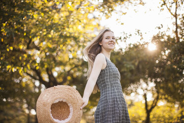 Teenage girl holding sunhat running in park - ISF14658