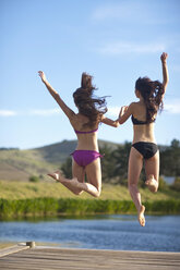 Two young women jumping from river pier - ISF14738