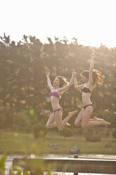 Two young women jumping off river pier - ISF14739