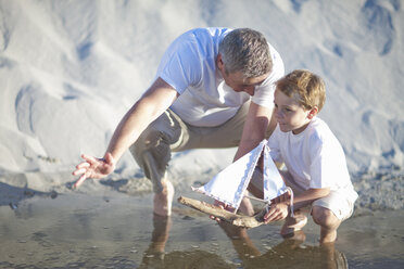 Vater und Sohn spielen Spielzeugboot am Strand - ISF14776