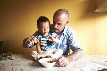 Kleiner Junge sitzt auf dem Tisch und isst Müsli mit seinem Vater - ISF14944