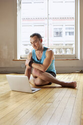 Mittlerer erwachsener Mann, der einen Laptop benutzt, während er die Cowface-Yoga-Pose einnimmt - ISF14955