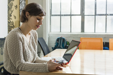 Young female designer texting on smartphone in design studio - ISF15044