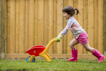 Junges Mädchen läuft mit Spielzeugschubkarre im Garten - ISF15110