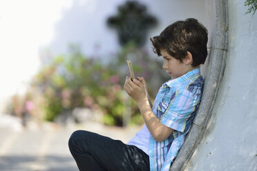 Boy leaning against curved wall texting on cellphone - ISF15114