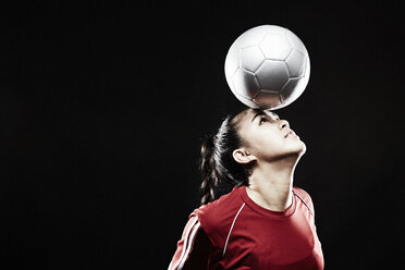 Young woman balancing football on forehead - ISF15126