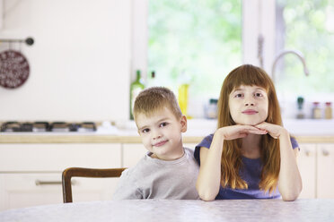 Portrait of sister and brother sitting at kitchen table - CUF37927