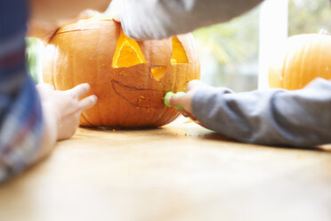 Siblings carving pumpkin in dining room - CUF38041