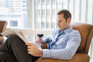 Mittlerer erwachsener Mann entspannt sich zu Hause mit Wein und Zeitung - ISF15163