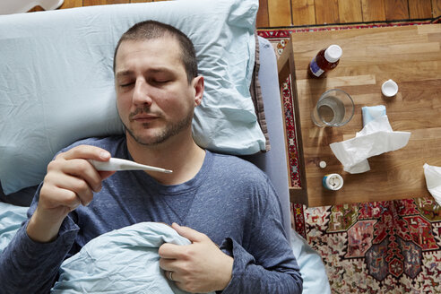 Mittlerer erwachsener Mann im Bett liegend mit Blick auf den Thermometerstand - ISF15265